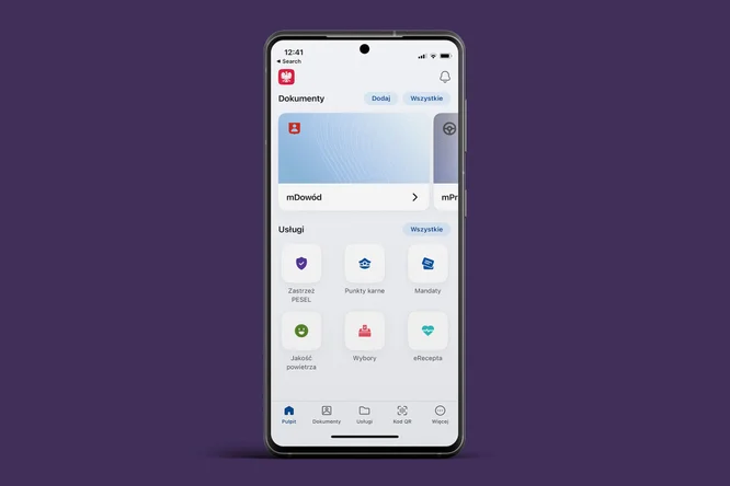 Na zdjęciu widoczny jest telefon komórkowy z wyświetlaczem w kolorze białym na tle fioletowym. Ekran telefonu przedstawia interfejs aplikacji, który zawiera różne ikony i przyciski. U góry znajduje się pasek wyszukiwania, a poniżej widoczne są kafelki z symbolami reprezentującymi różne funkcje lub kategorie, takie jak finanse, zakupy czy usługi. Całość ma nowoczesny, przejrzysty wygląd.