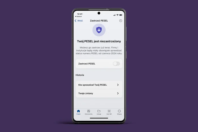 Na zdjęciu widoczny jest telefon komórkowy z białym wyświetlaczem na tle fioletowym. Ekran przedstawia interfejs aplikacji dotyczącej zarządzania numerem PESEL. U góry widnieje ikona z tarczą oraz napis "Zastrzeż PESEL". Poniżej znajduje się informacja, że PESEL jest niezastrzeżony, a także przycisk do zastrzeżenia numeru. Dodatkowo, sekcja "Historia" informuje o tym, kto zarządzał numerem PESEL oraz o zmianach. Na dole ekranu znajdują się ikony reprezentujące różne funkcje aplikacji.