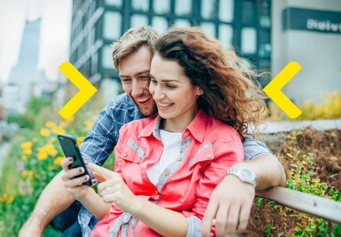 Para siedzi na ławce przed biurowcem i śmieje się do telefonu