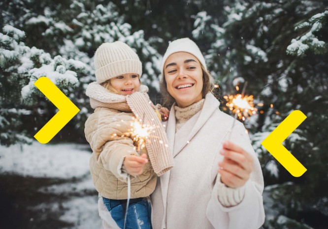 Matka z dzieckiem odpala zimne ognie na zewnątrz. W tle widać ośnieżone drzewa.