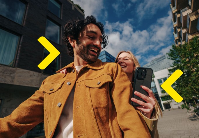 Kobieta ciepło ubrana siedzi na ławce w parku w jesiennej aurze i uśmiecha się do telefonu