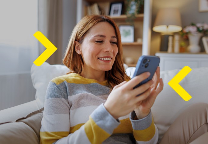 Kobieta siedząca na kanapie w mieszkaniu i uśmiechająca się do swojego telefonu