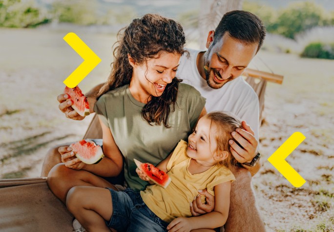 Trzyosobowa rodzina siedzi na plaży na hamaku i je arbuza