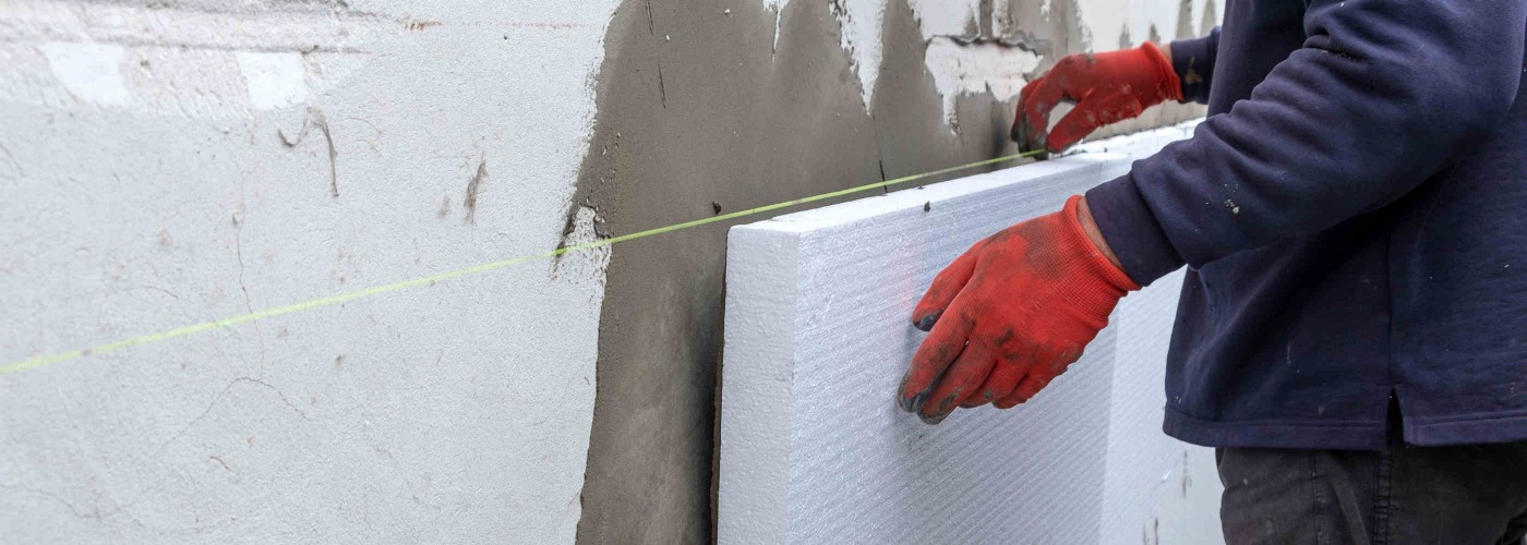 Construction worker installing styrofoam insulation sheets on house facade wall for thermal protection.