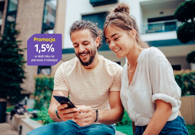 Para damsko-męska siedzi na murku przed blokiem i patrzy w telefon, śmiejąc się