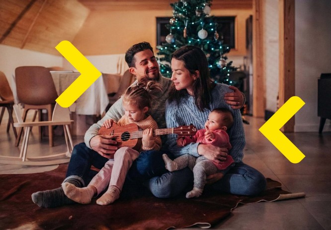 Czteroosobowa rodzina siedzi na podłodze w salonie, przytulając się. Dziewczynka ma gitarę na kolanach. W tle widać choinkę.
