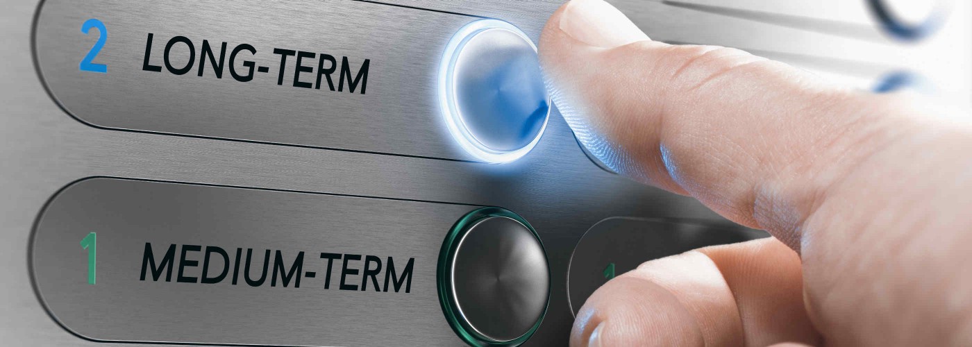 Zdjęcie przedstawia rękę naciskającą przycisk na panelu sterowania, z podświetleniem i oznaczeniami "LONG-TERM" i "MEDIUM-TERM"