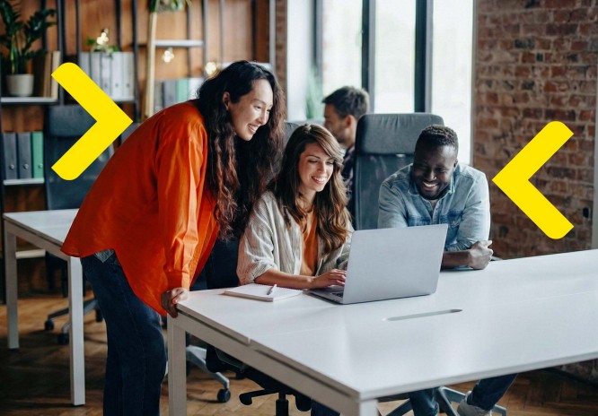 Das Bild zeigt eine Frau, die an einem Schreibtisch steht und eine Tasse hält. Vor ihr befindet sich ein Laptop, und im Hintergrund sind helle Fenster mit Blick auf die Stadt sichtbar. Das Interieur ist modern, mit warmem Licht und stilvollen Möbeln, was eine gemütliche Atmosphäre schafft. Die Frau trägt eine rote Bluse, die der gesamten Komposition Farbe verleiht.